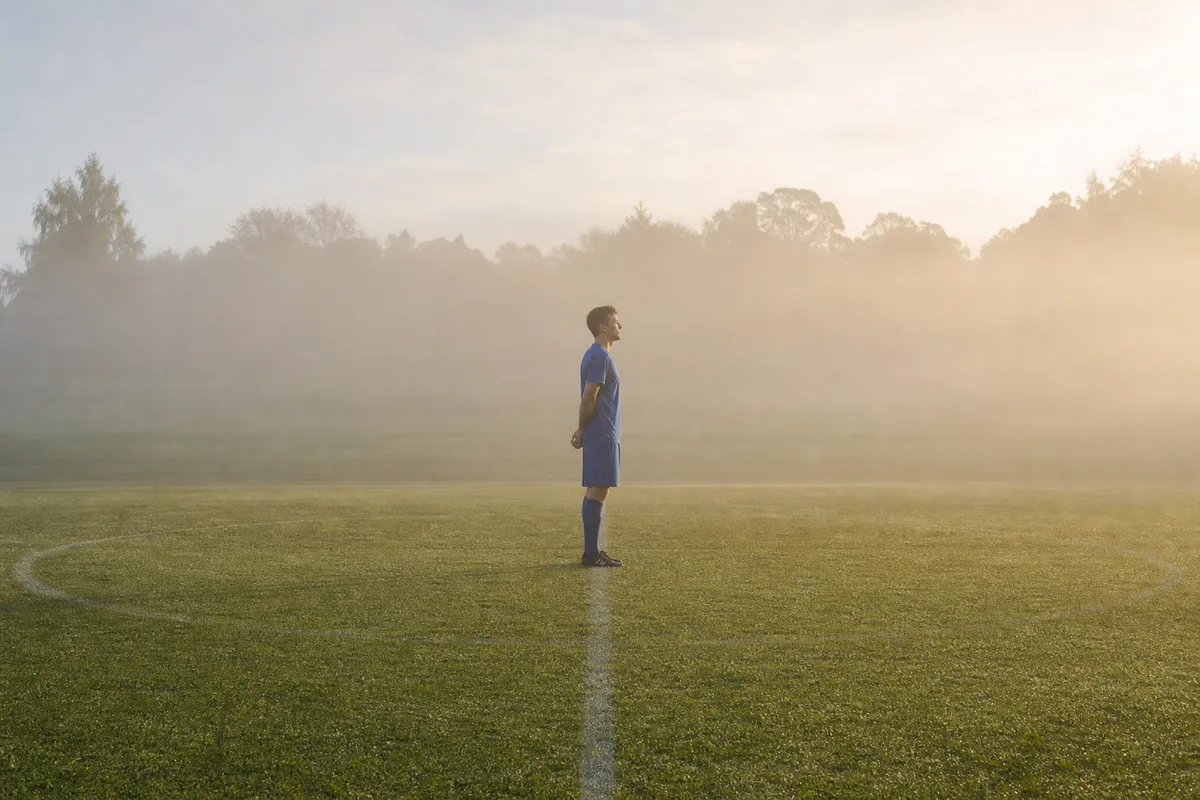 Joueur de football seul de profil sur le terrain, yeux fermés, en respiration de préparation avant le coup d’envoi