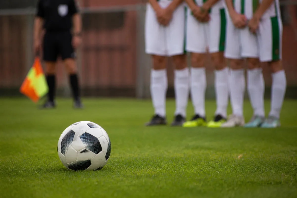 Ballon posé sur l&rsquo;herbe devant un mur de joueurs, arbitre assistant drapeau baissé en arrière-plan